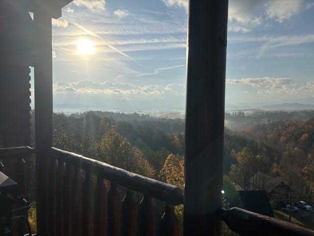 A sunrise framed by the pillars and handrails of a porch. The sun rises on the horizon casting rays of light over the forest.
